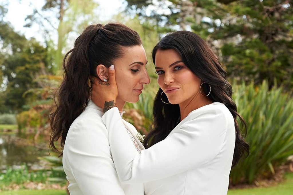 two woman in white suits embrace as one looks at the camera
